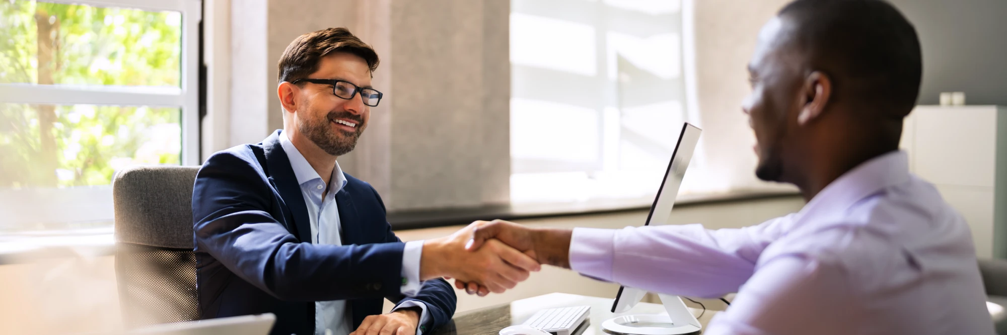 Two men shaking hands at a desk
