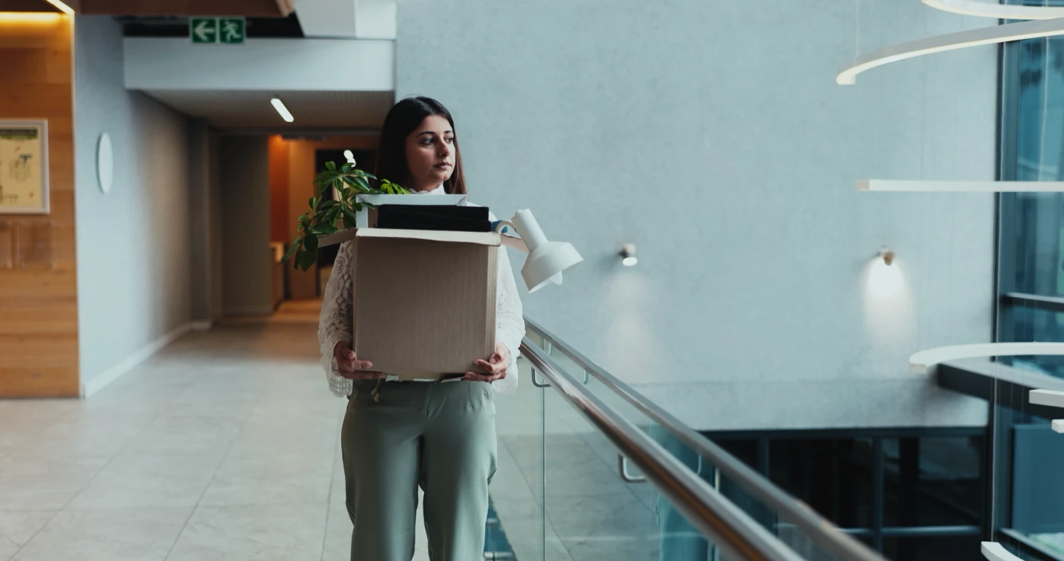 A woman carrying a box through an office hallway