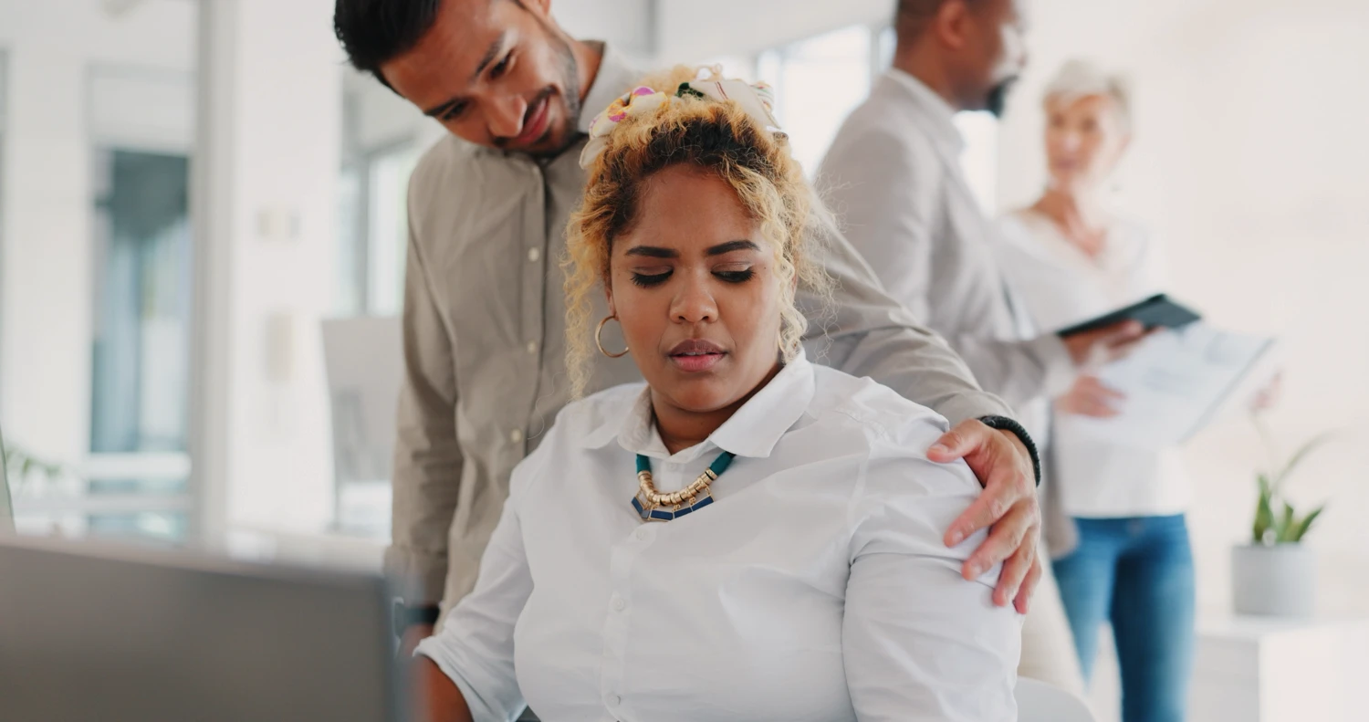 A woman looking uncomfortable with a male coworker touching her shoulder