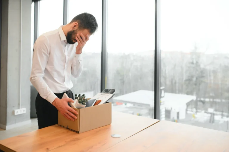 A man looking distressed in an office with a box packed full of office supplies