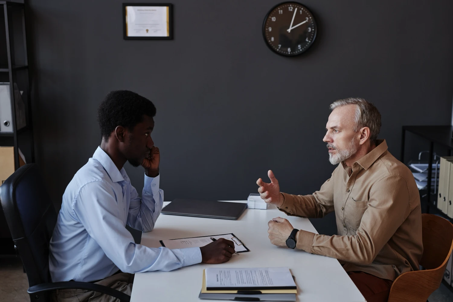Two men sitting at a desk and talking over documents