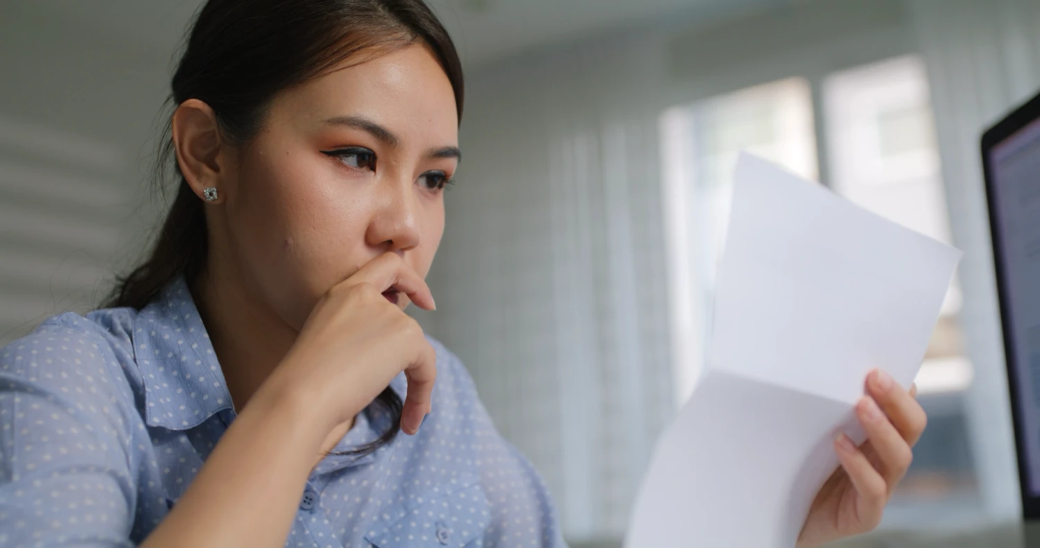 Young female worker frowning at a letter notifying her that she's been fired